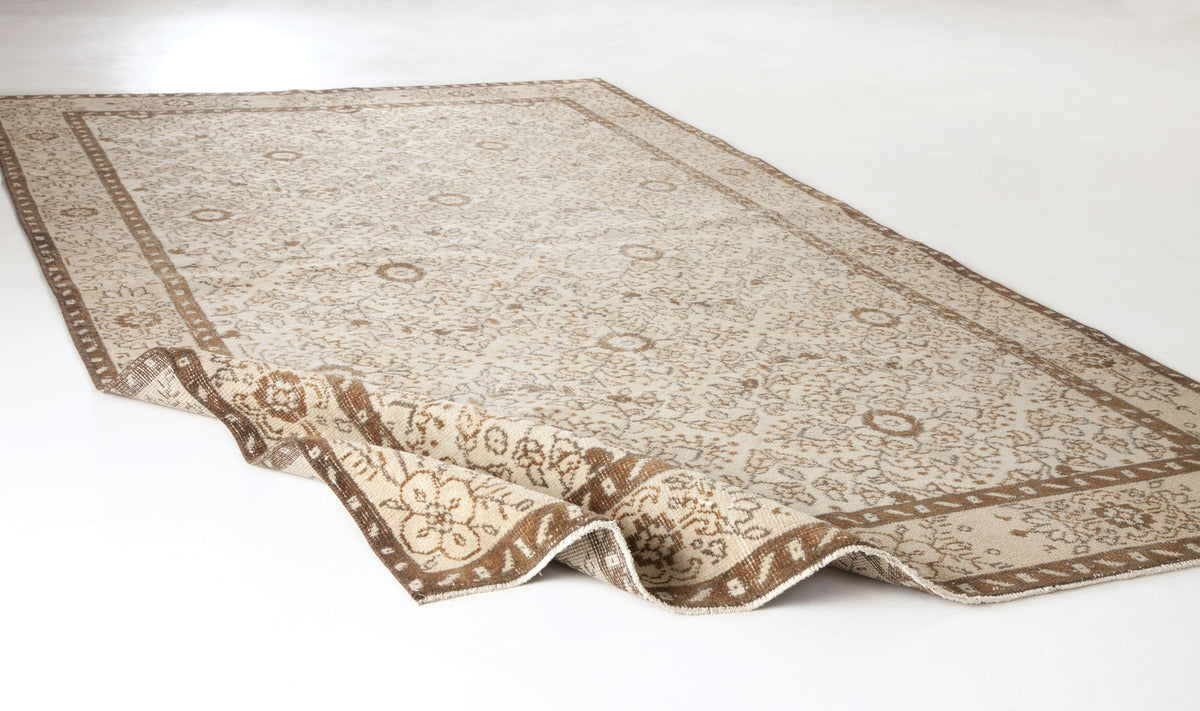 Beige and brown traditional rug with a floral medallion pattern and a folded corner on a white background.