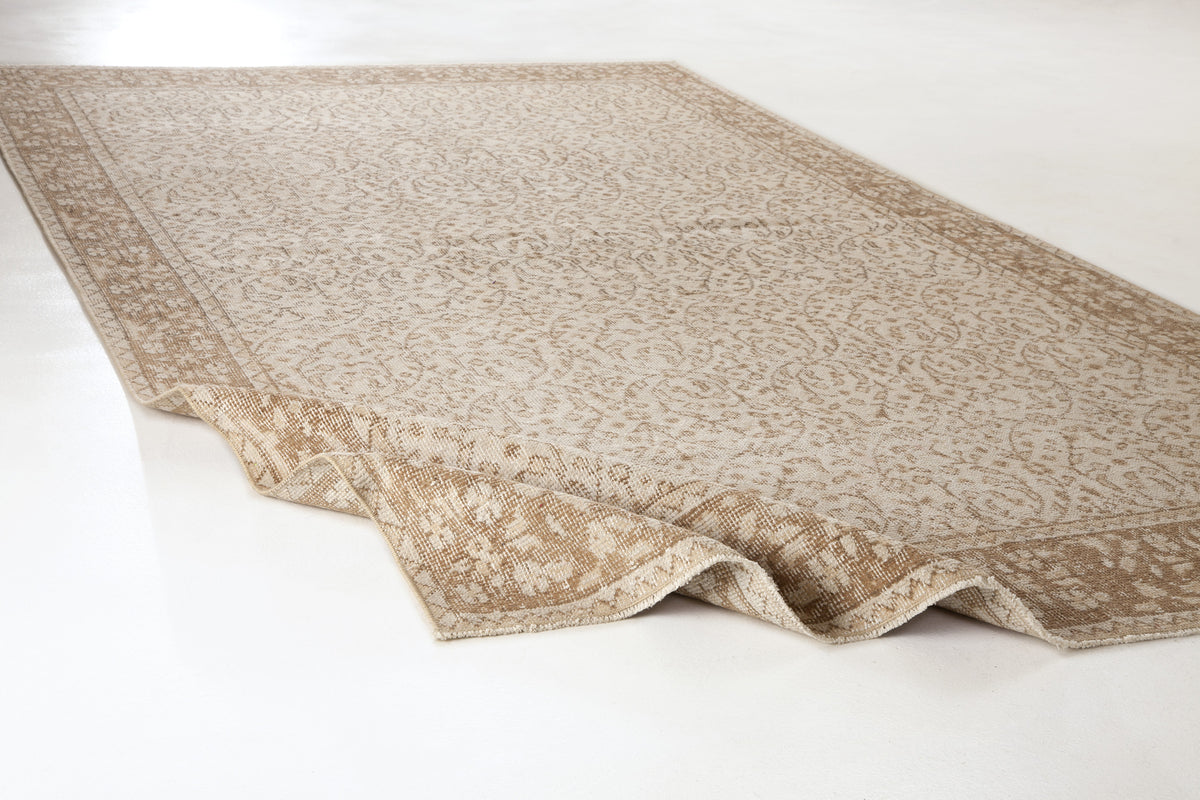 Beige and cream area rug with a traditional floral pattern and a wide border, shown with one corner folded over.