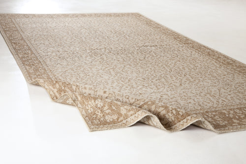 Load image 1 in gallery view. Beige and cream area rug with a traditional floral pattern and a wide border, shown with one corner folded over.