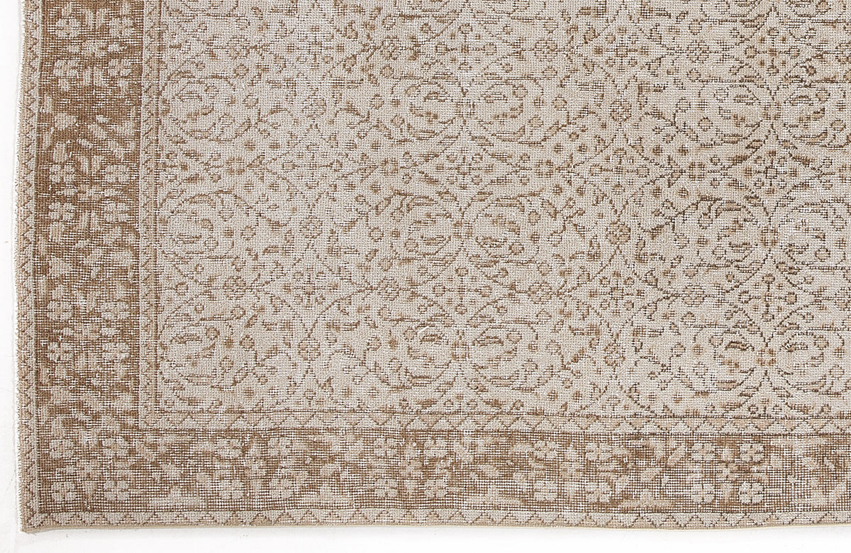 Beige and tan rug with a distressed traditional floral vine pattern and a wide decorative border.