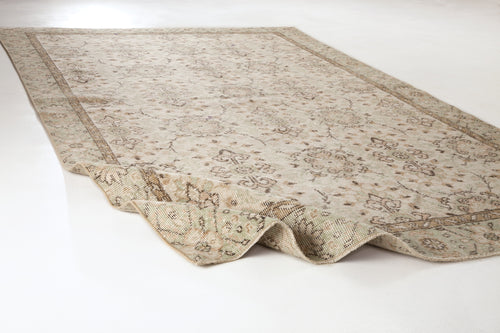 Load image 1 in gallery view. Beige and cream vintage-style rug with a faded floral medallion pattern and a folded corner on a white background.