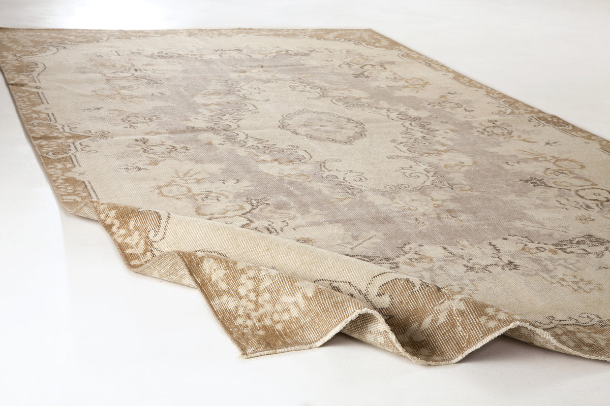 Beige and taupe distressed traditional rug with a central medallion and floral border on a white background.