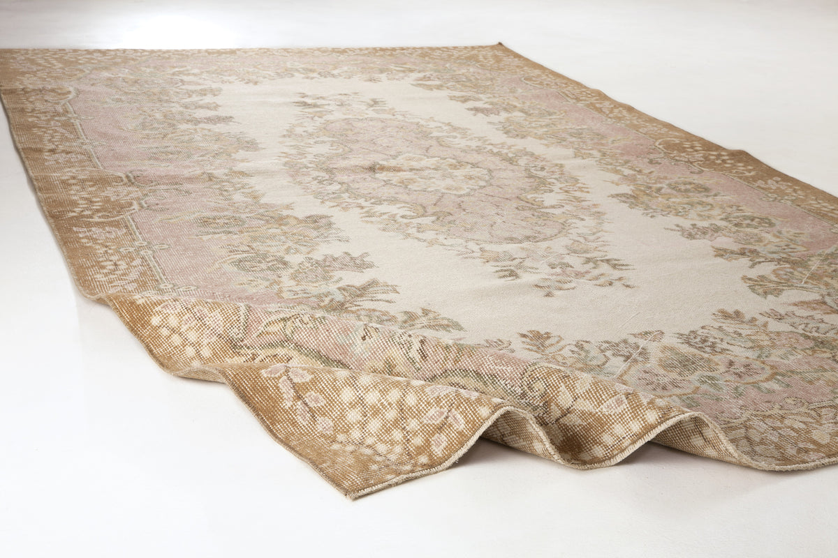 Beige and pale pink vintage-style rug with a central floral medallion and ornate border on a white background.