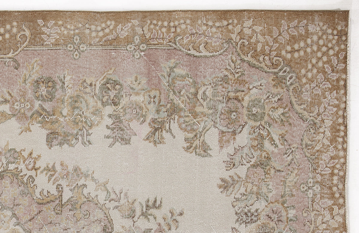 Distressed beige and dusty pink rug with a faded floral medallion pattern and ornate border.