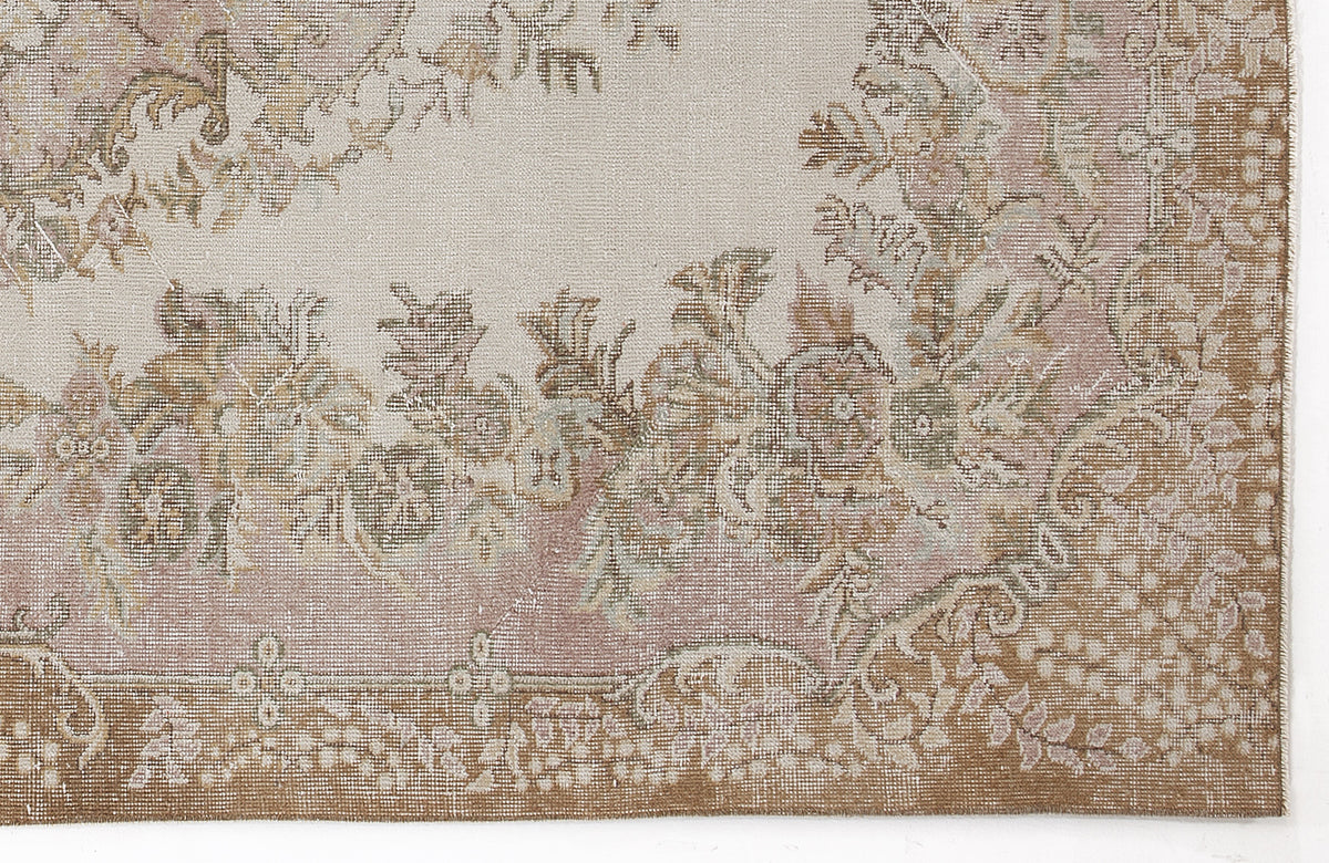 Distressed beige and dusty rose rug with a traditional floral medallion pattern and a wide brown border.