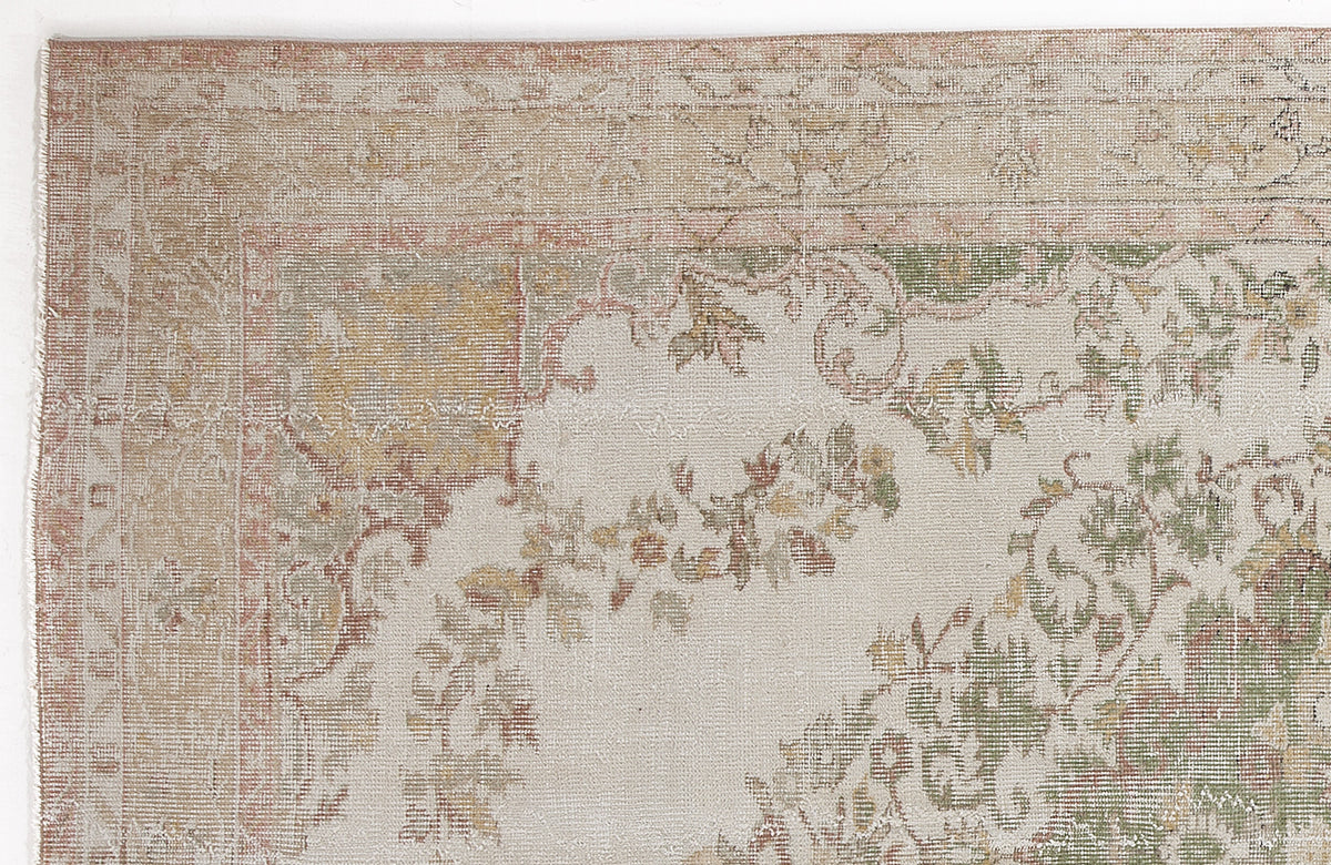 Distressed beige rug with faded floral motifs in muted green, gold, and terracotta, featuring a traditional border.