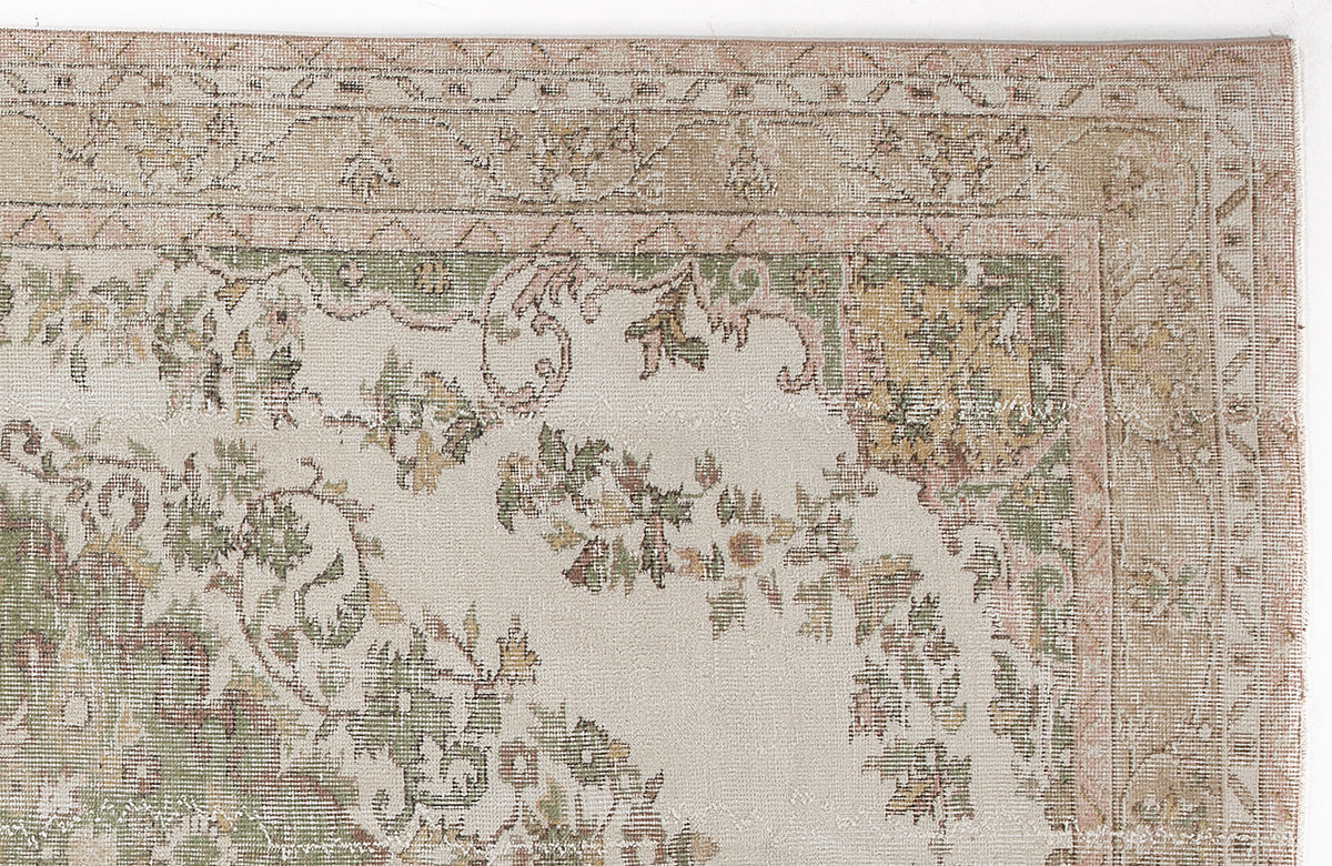 Beige rug with a muted green, pink, and tan floral border and central medallion pattern on a cream background.