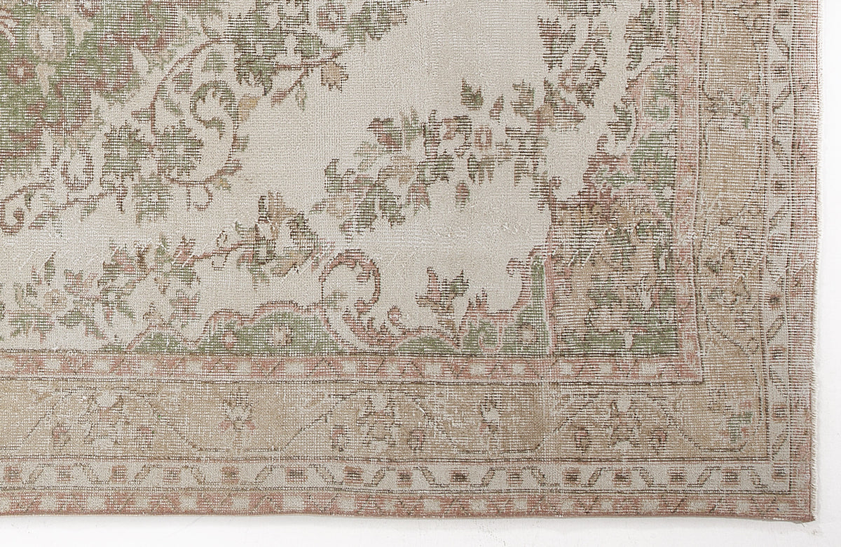 Cream rug with a distressed floral medallion pattern in sage green and muted terracotta, featuring a geometric border.