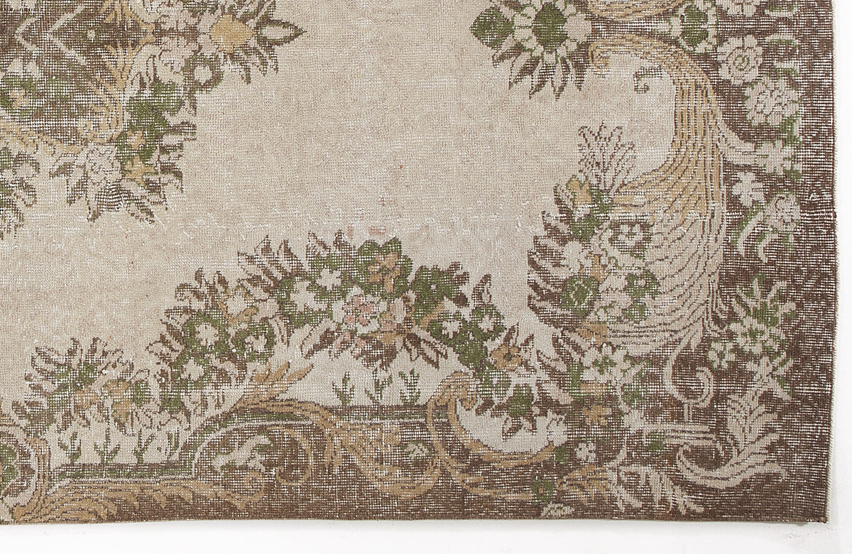 Beige rug with a distressed brown and green floral medallion pattern and ornate border.