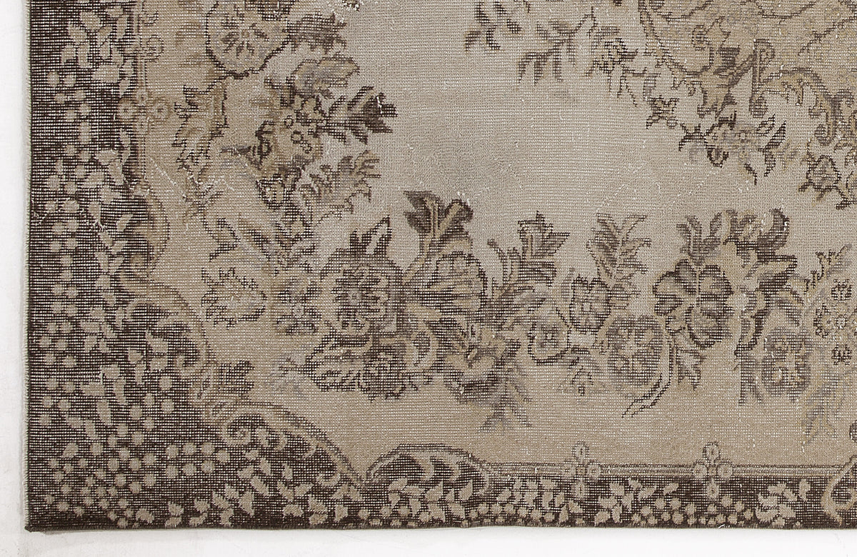 Taupe and dark brown rug with a distressed floral medallion pattern and ornate border.