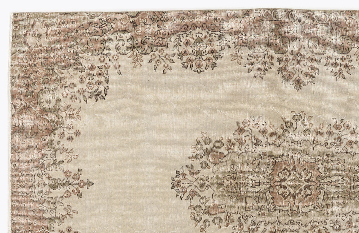 Beige rug with a distressed floral medallion pattern in muted terracotta and sage green.