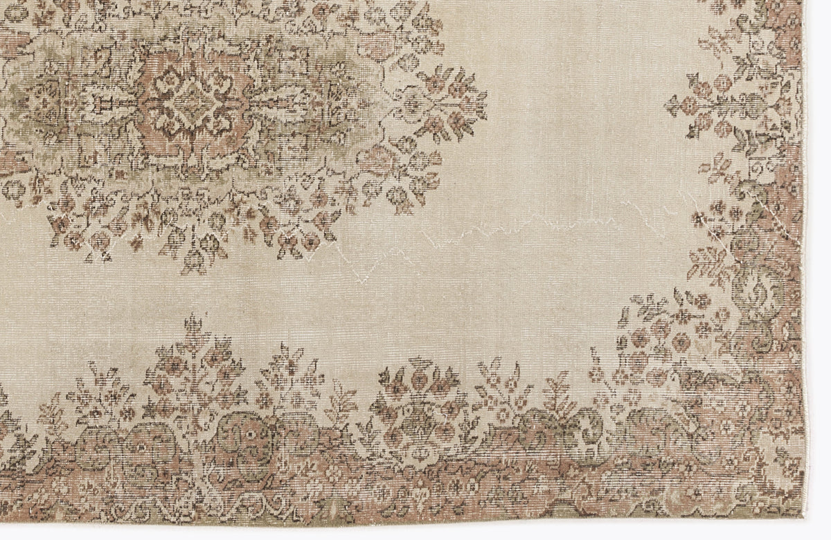 Beige rug with a distressed floral medallion and border pattern in muted sage green and dusty rose.