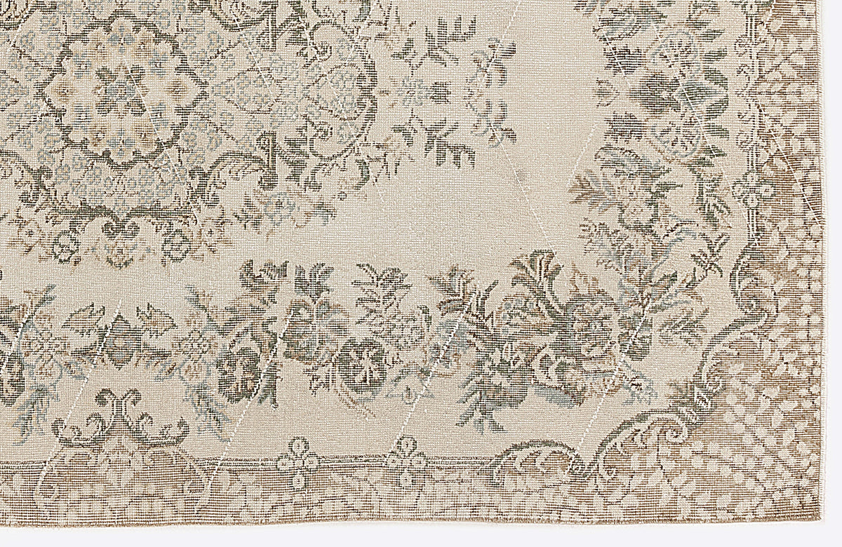 Beige rug with a distressed floral medallion pattern in muted olive, blue, and brown tones on a white background.