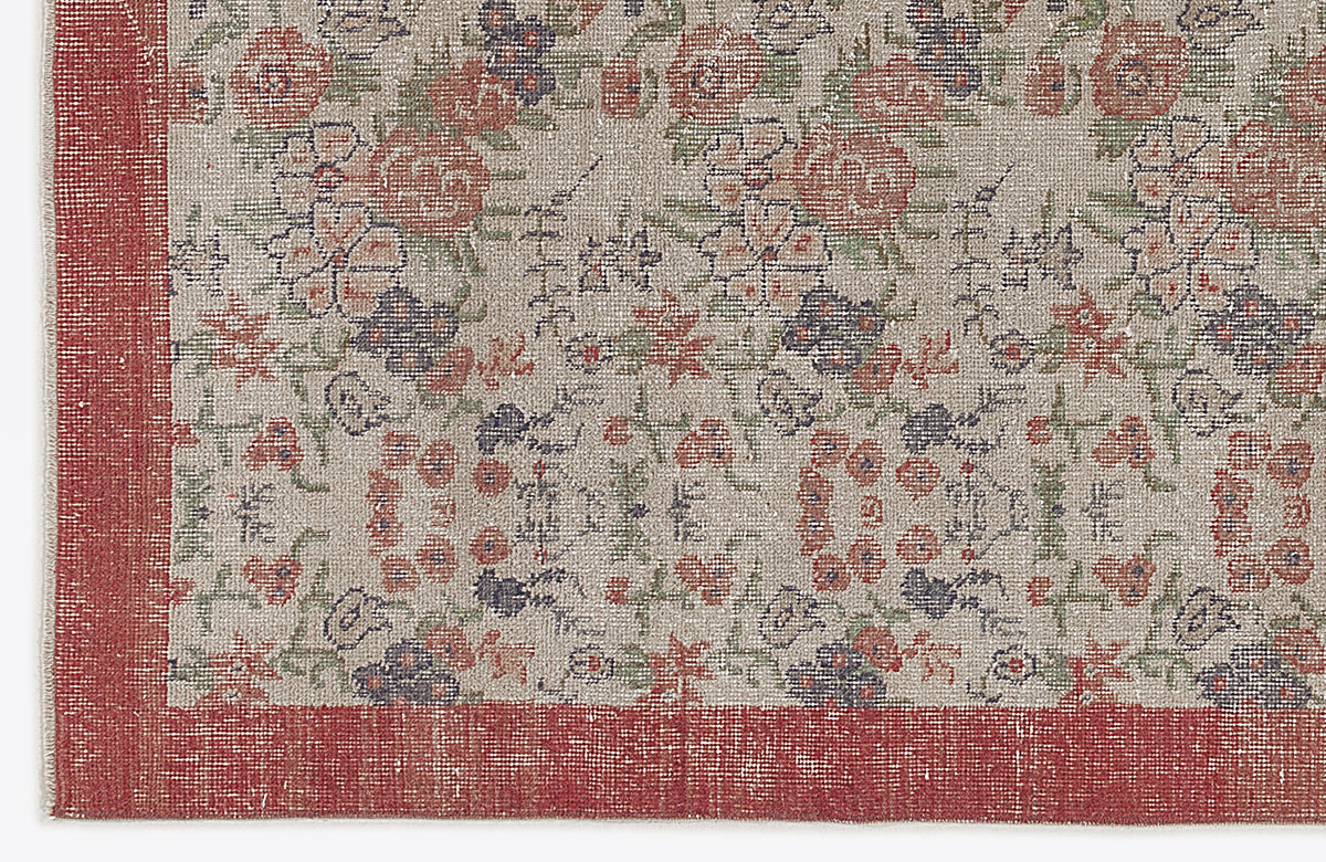 Beige rug with a distressed floral pattern in red, green, and dark blue, featuring a solid red border.