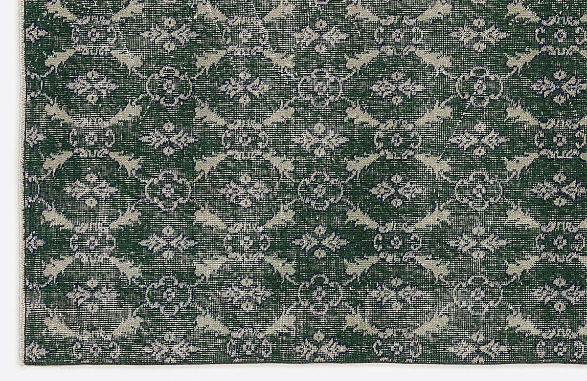Dark green rug with a repeating light grey floral medallion pattern and a distressed, vintage-style finish.