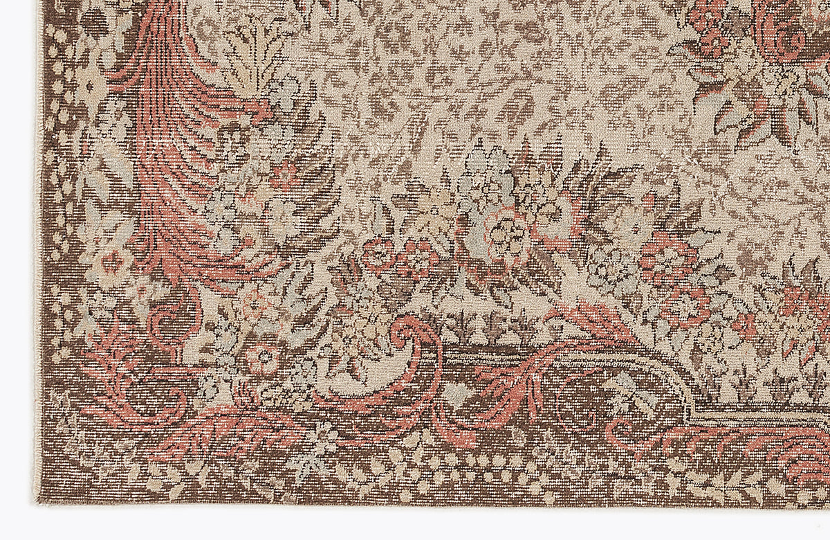 Close-up of a traditional rug with a distressed floral medallion pattern in shades of brown, cream, and muted coral.