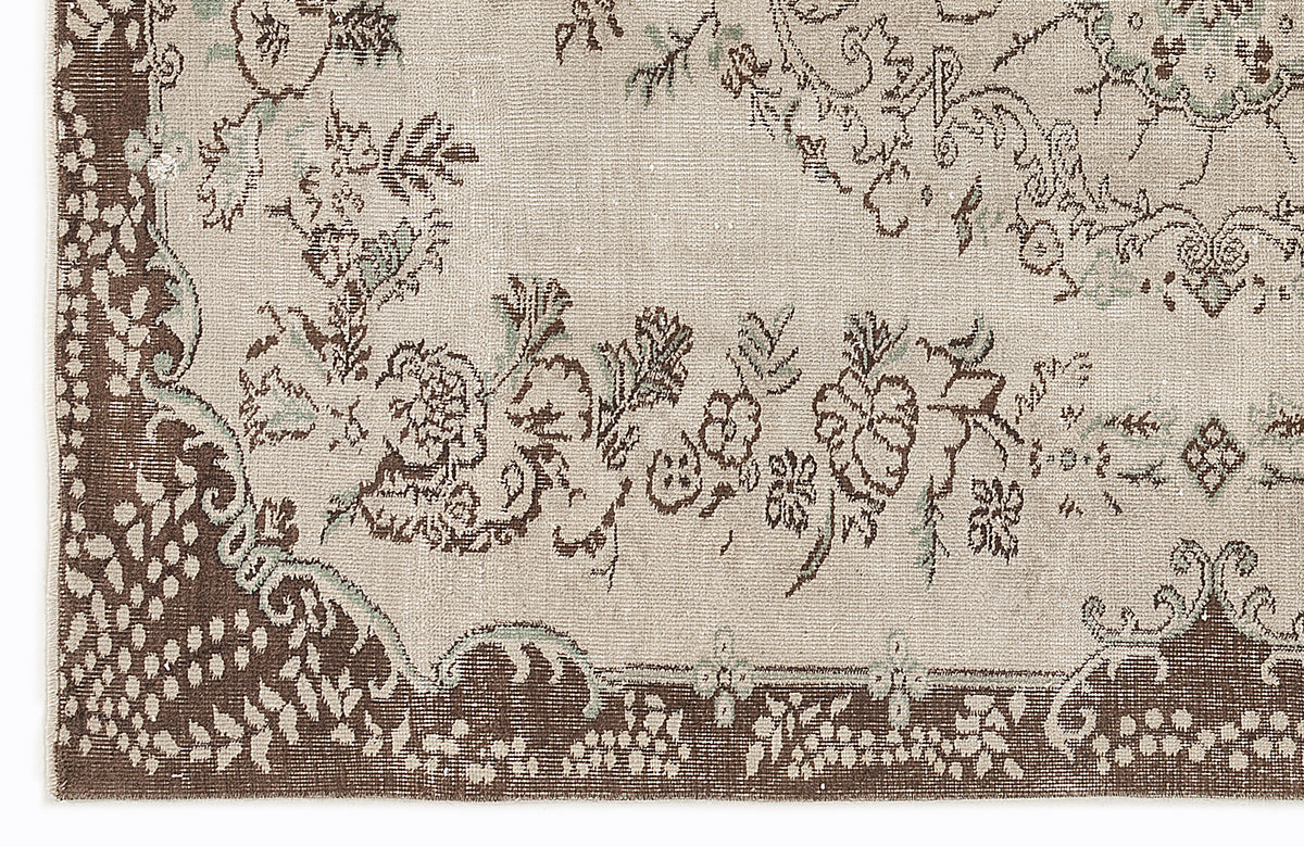 Beige and brown rug with a distressed floral medallion pattern and sage green accents.