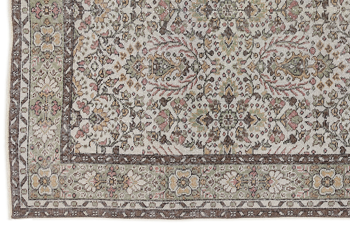 Distressed traditional rug with a floral medallion pattern in muted sage, pink, and brown on a cream background.