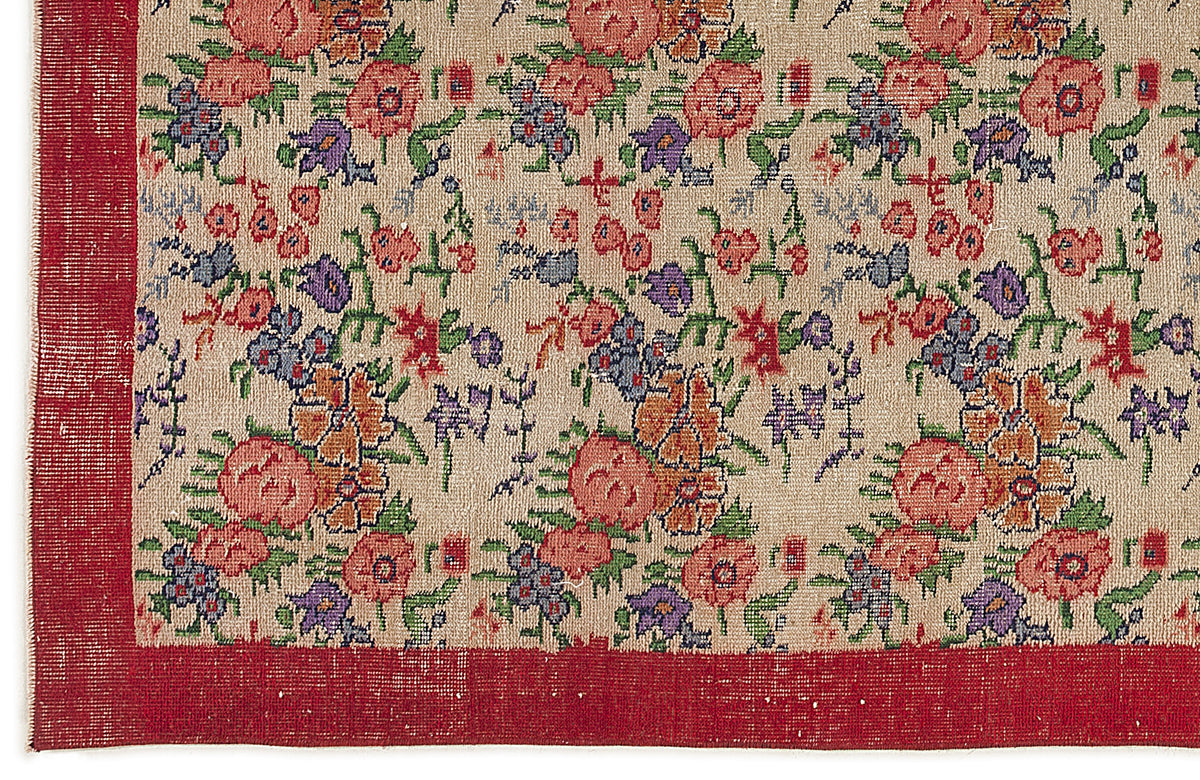 Beige rug with a repeating floral pattern in red, purple, and green, featuring a solid red border.