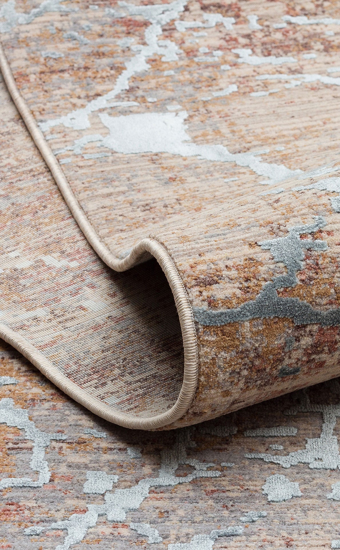Beige, rust, and light blue abstract distressed rug with a rolled corner showing a finished edge.