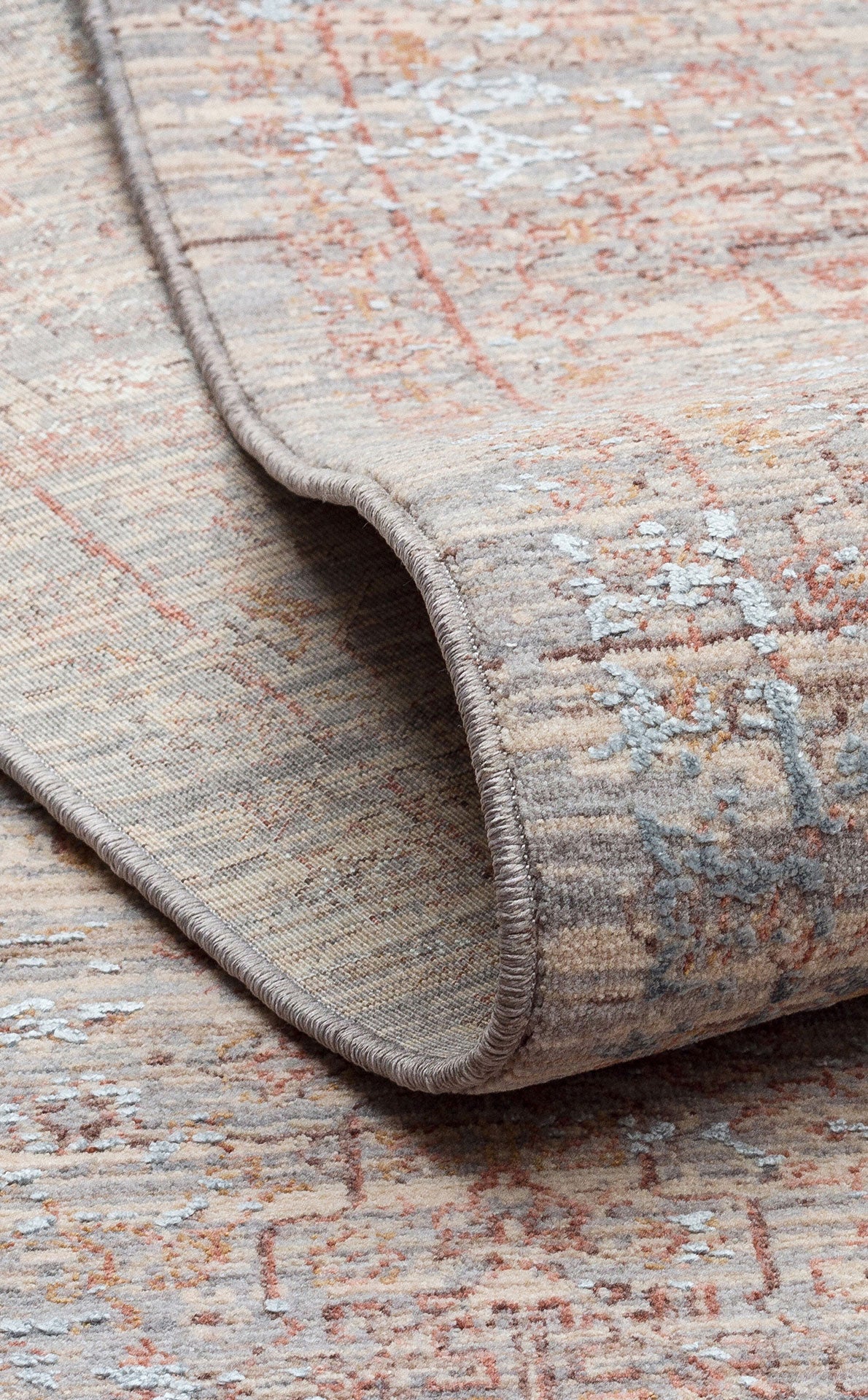 Beige and grey distressed rug with a faded traditional pattern and rust-colored accents, shown with a folded corner.
