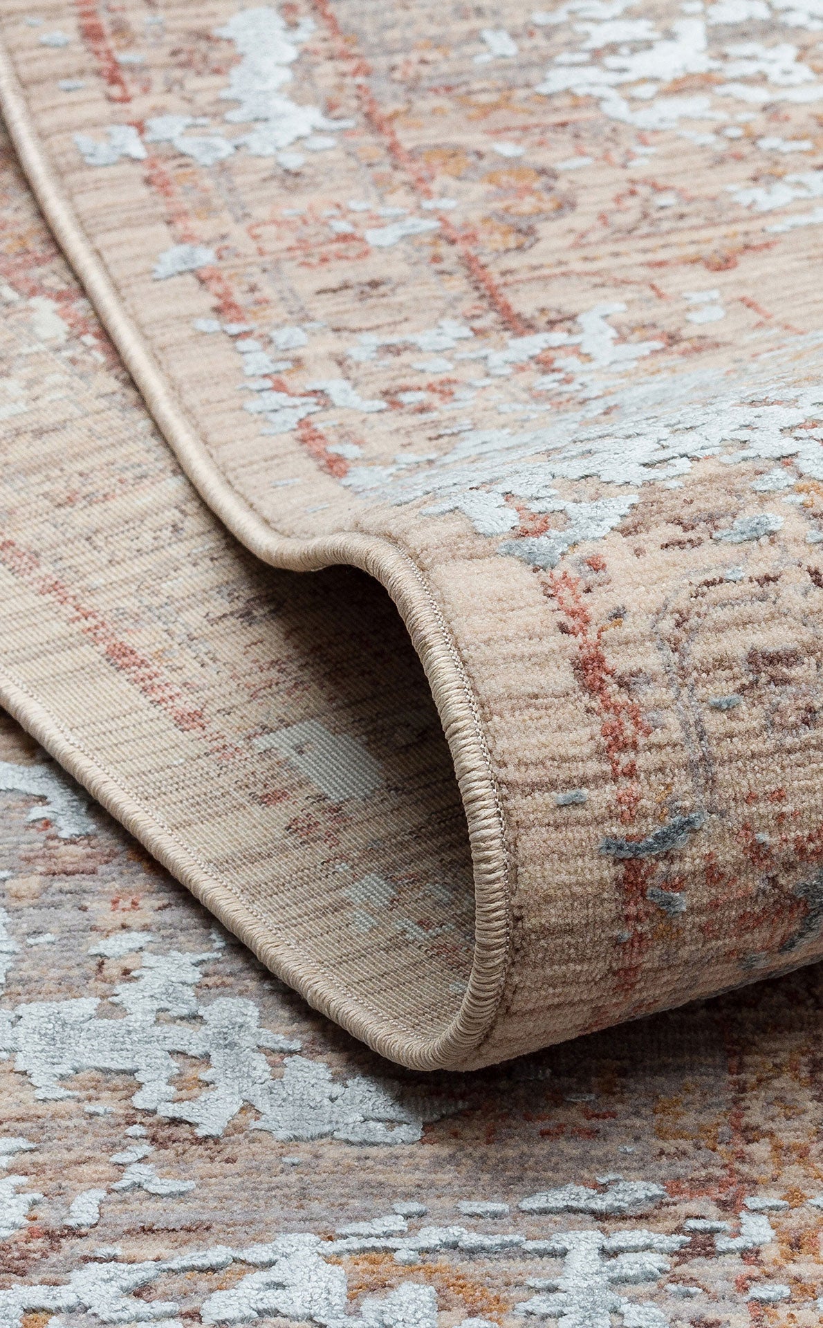 Beige and rust-colored rug with a distressed, faded traditional pattern and light blue accents, shown folded.