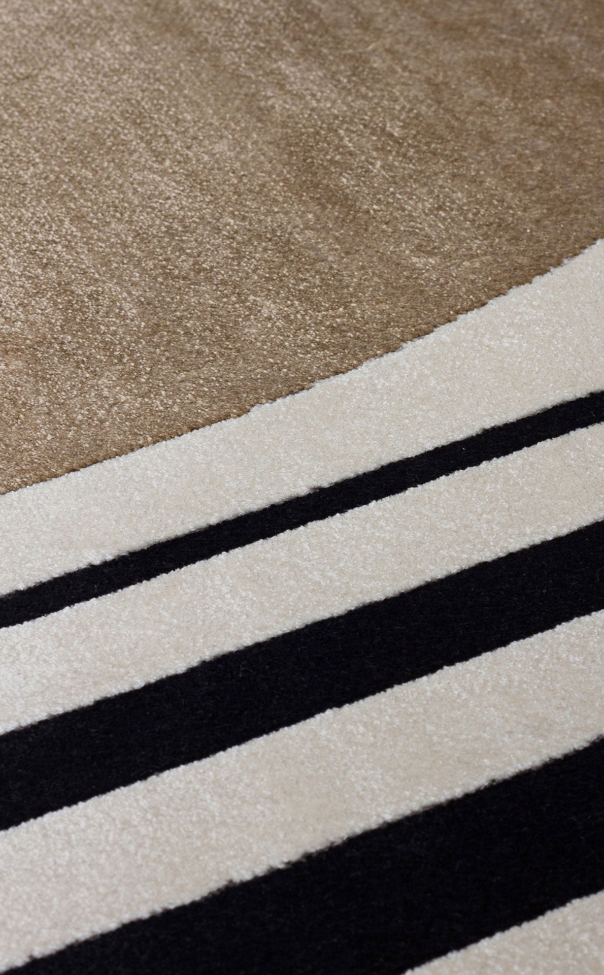 Close-up of a rug featuring a large tan section transitioning into bold black and cream horizontal stripes.