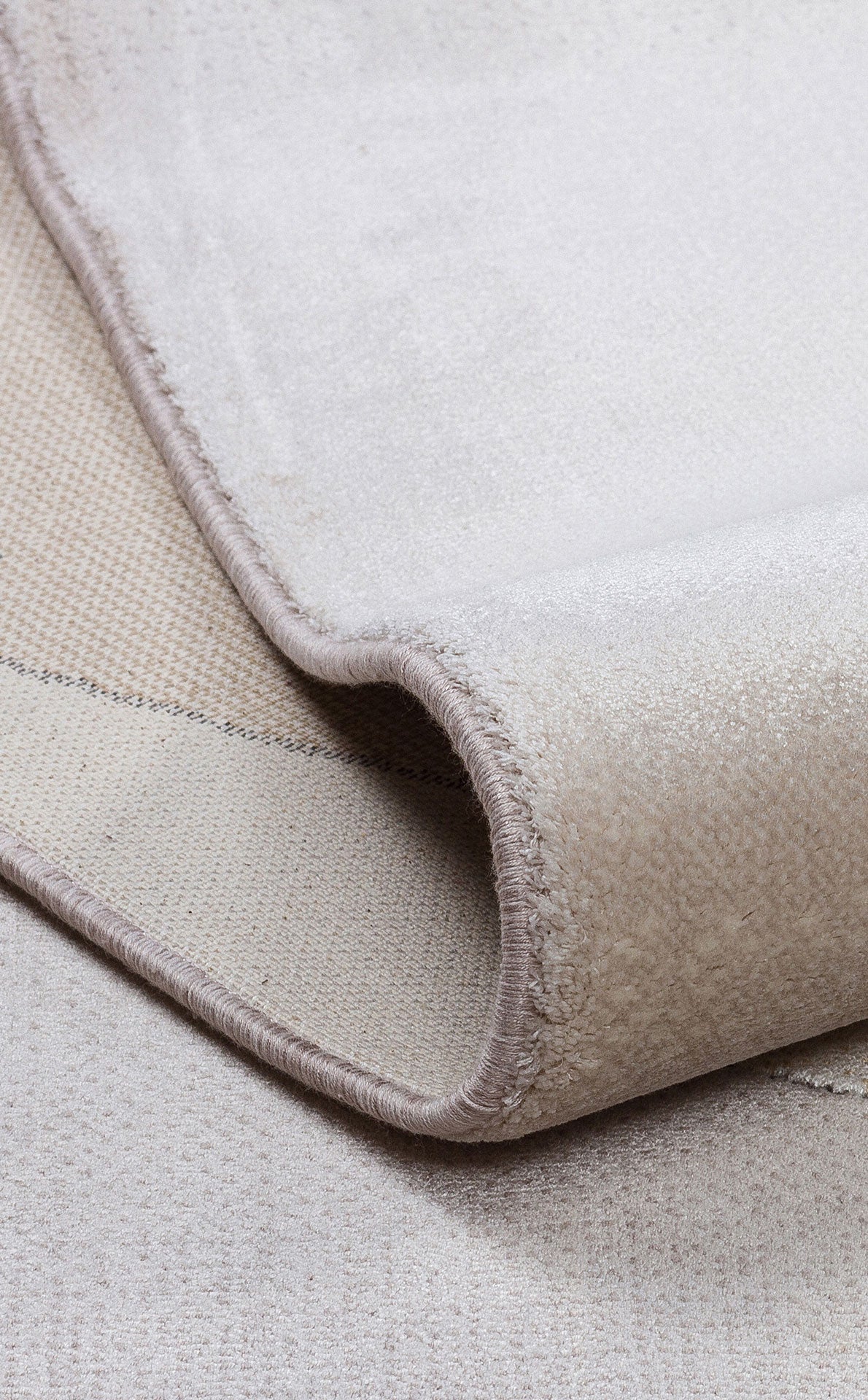 Solid beige rug with a soft, velvet-like texture and finished serged edges, shown folded to reveal the woven backing.