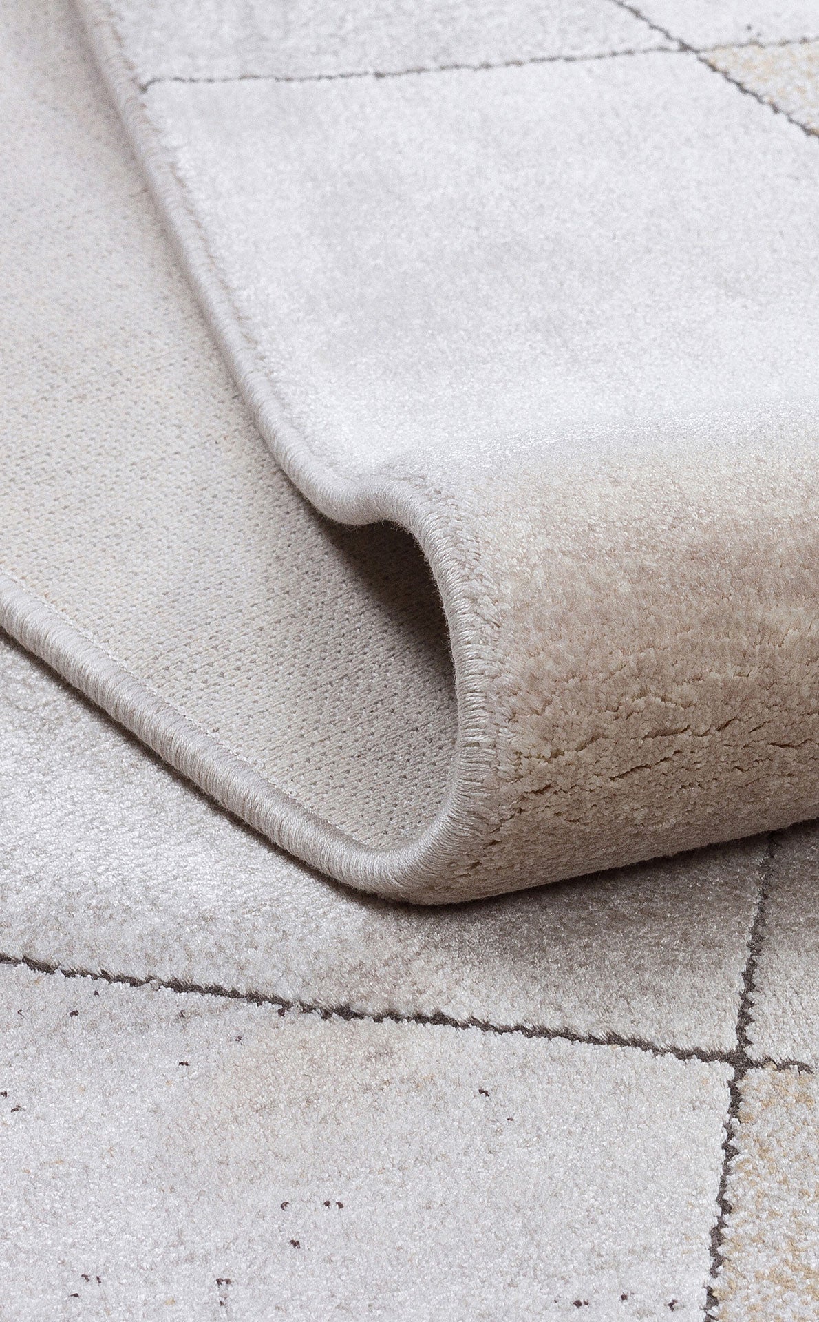 Beige and cream rug with a subtle grid pattern, shown folded to reveal the pile texture and finished edge.