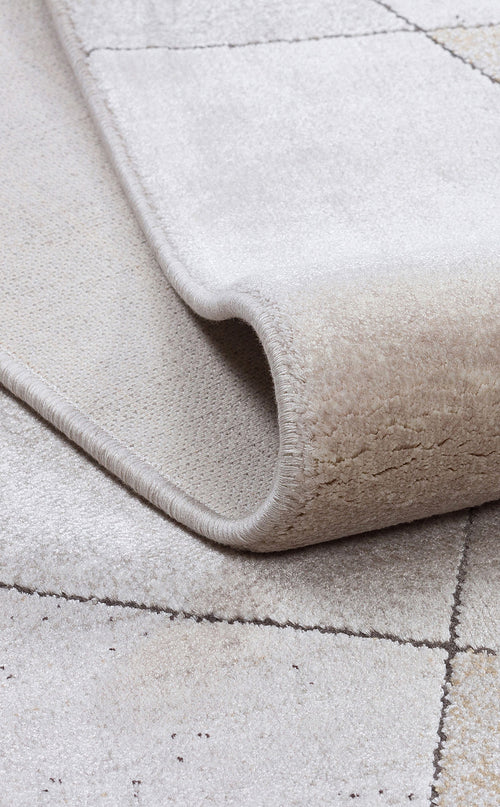 Bild 1 in Galerieansicht laden. Beige and cream rug with a subtle grid pattern, shown folded to reveal the pile texture and finished edge.