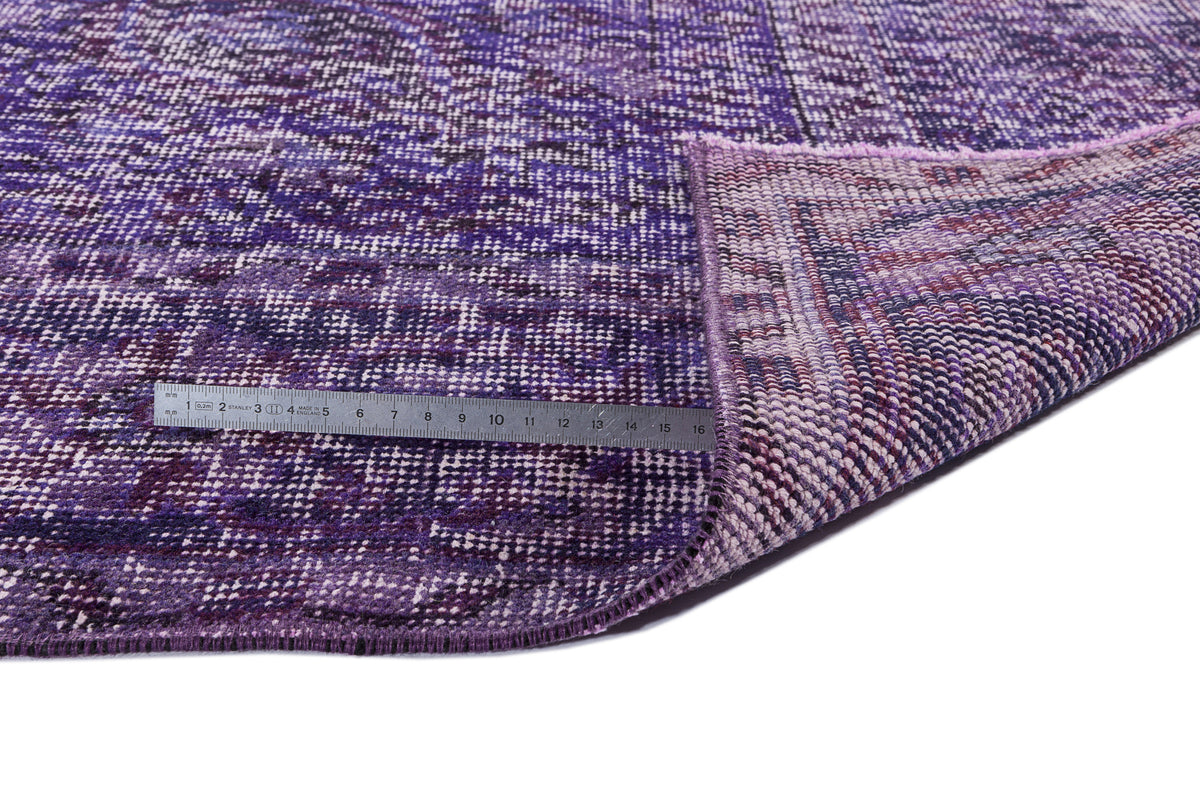 Deep purple distressed vintage-style rug with a folded corner and a metal ruler for scale on a white background.
