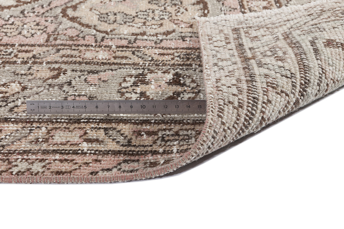 Distressed pink, brown, and cream medallion rug with a folded corner and a metal ruler for scale on a white background.