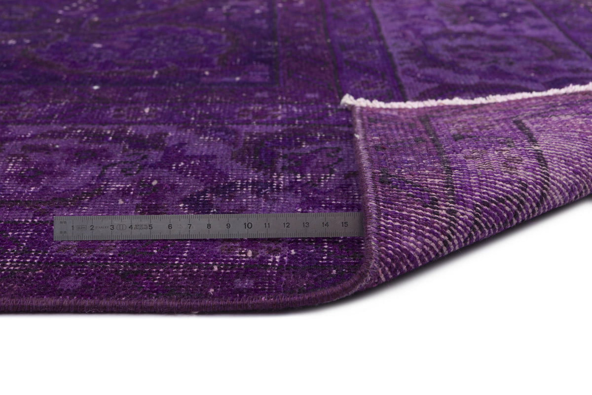 Deep purple distressed rug with a traditional medallion pattern, shown with a corner folded over and a metal ruler.