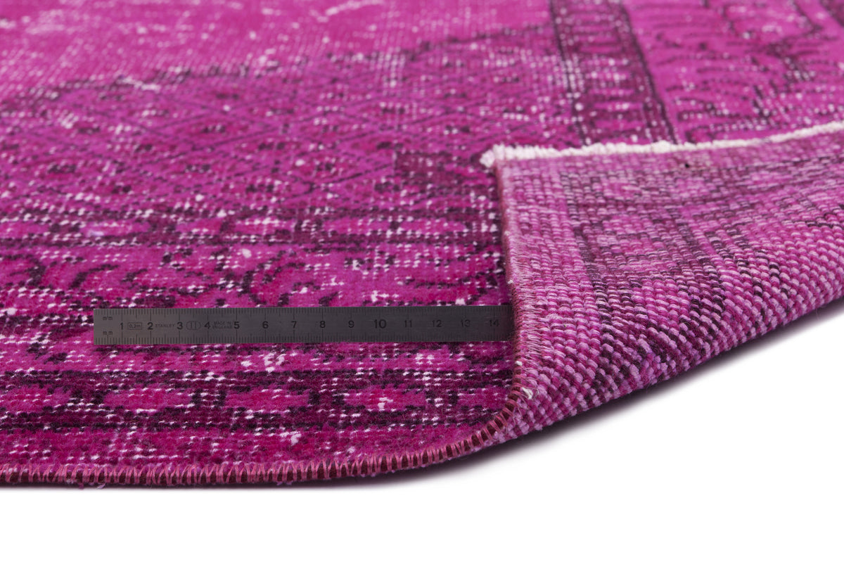 Magenta and black distressed vintage-style rug with a folded corner and a metal ruler for scale on a white background.