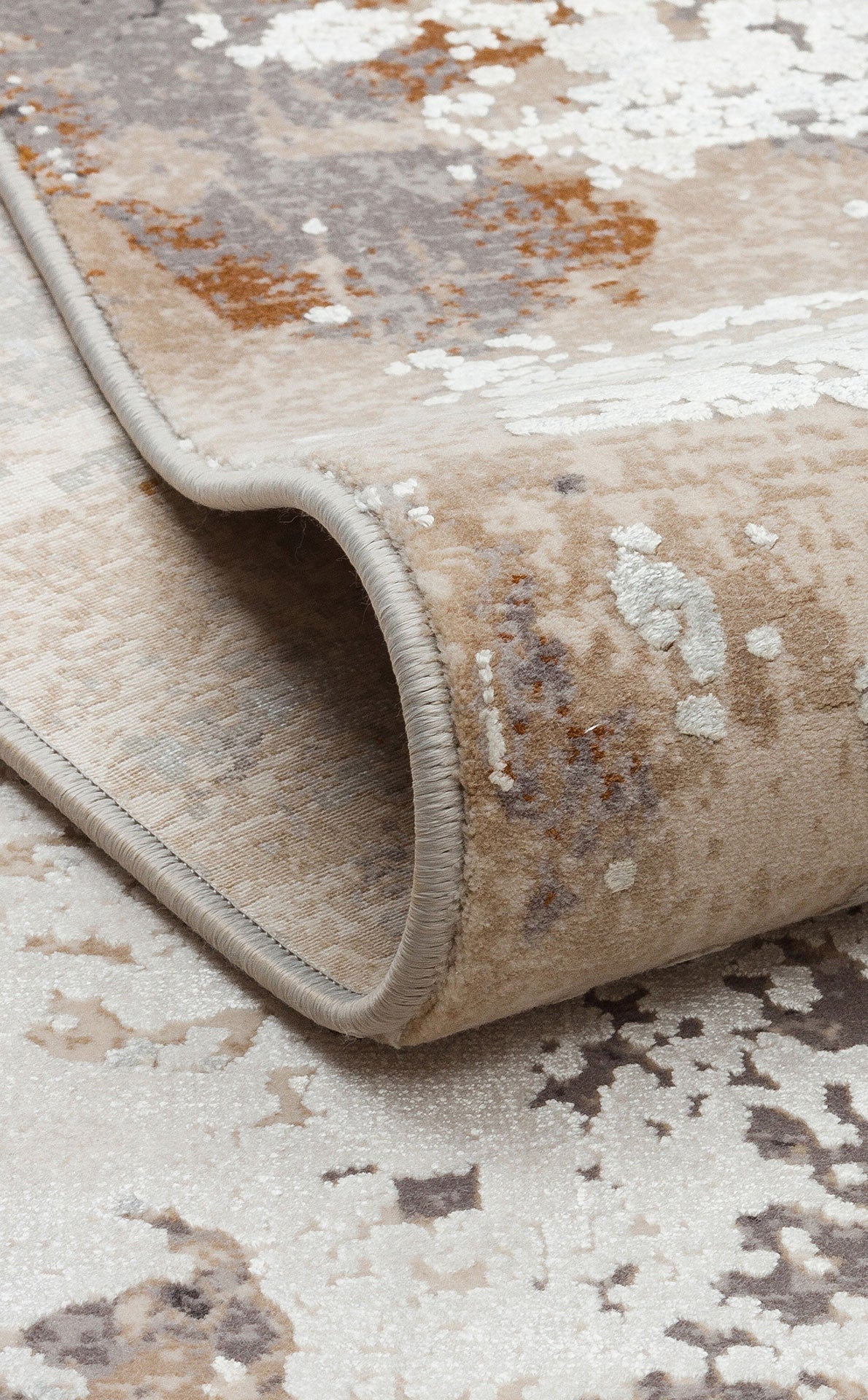 Beige, grey, and white abstract distressed rug with a folded corner showing serged edges.