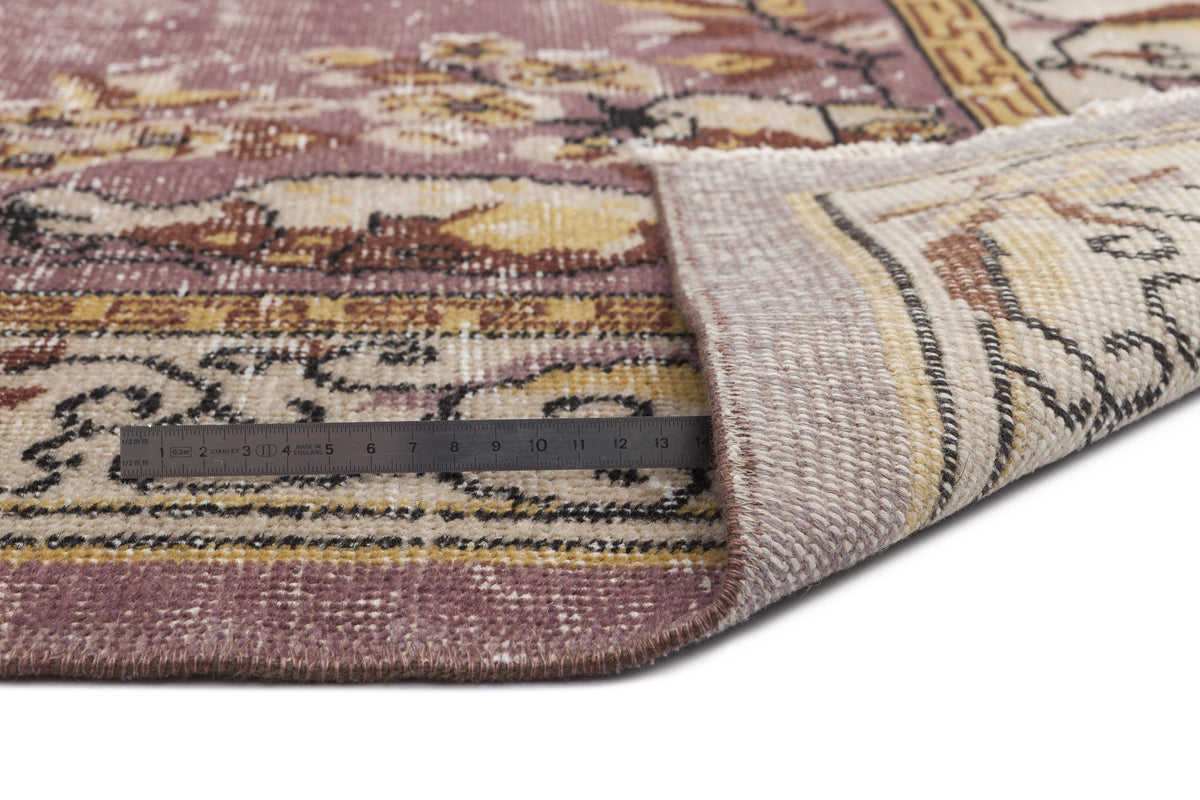 Distressed mauve and beige rug with a floral medallion pattern, shown folded with a metal ruler for scale.