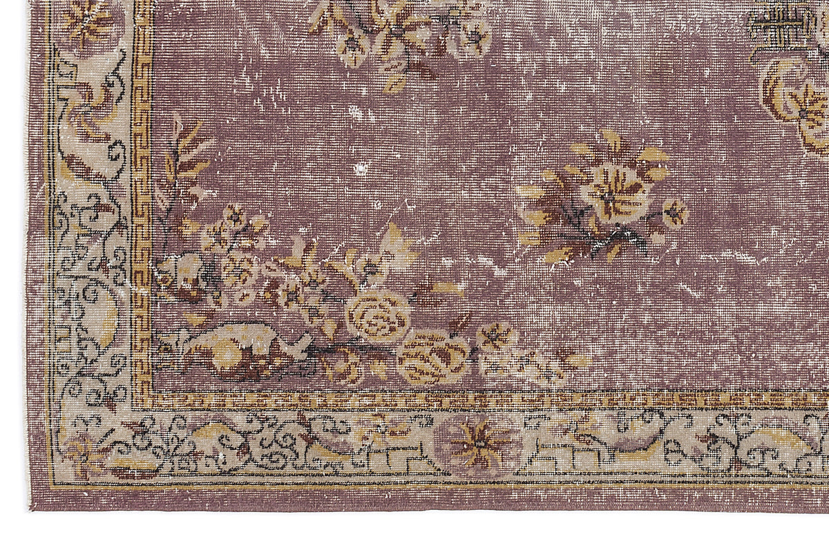 Distressed mauve rug with a beige border, featuring a floral pattern and geometric Greek key accents.