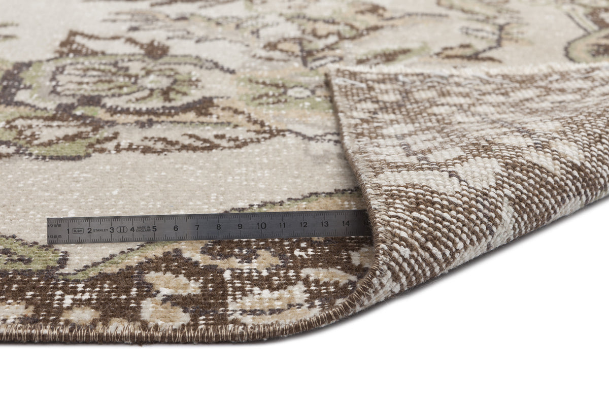 Beige and brown floral patterned rug with a folded corner showing the woven backing and a metal ruler for scale.