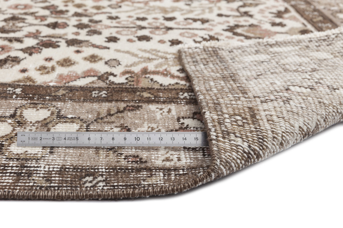 Beige and brown traditional patterned rug with a folded corner revealing the woven backing and a metal ruler for scale.