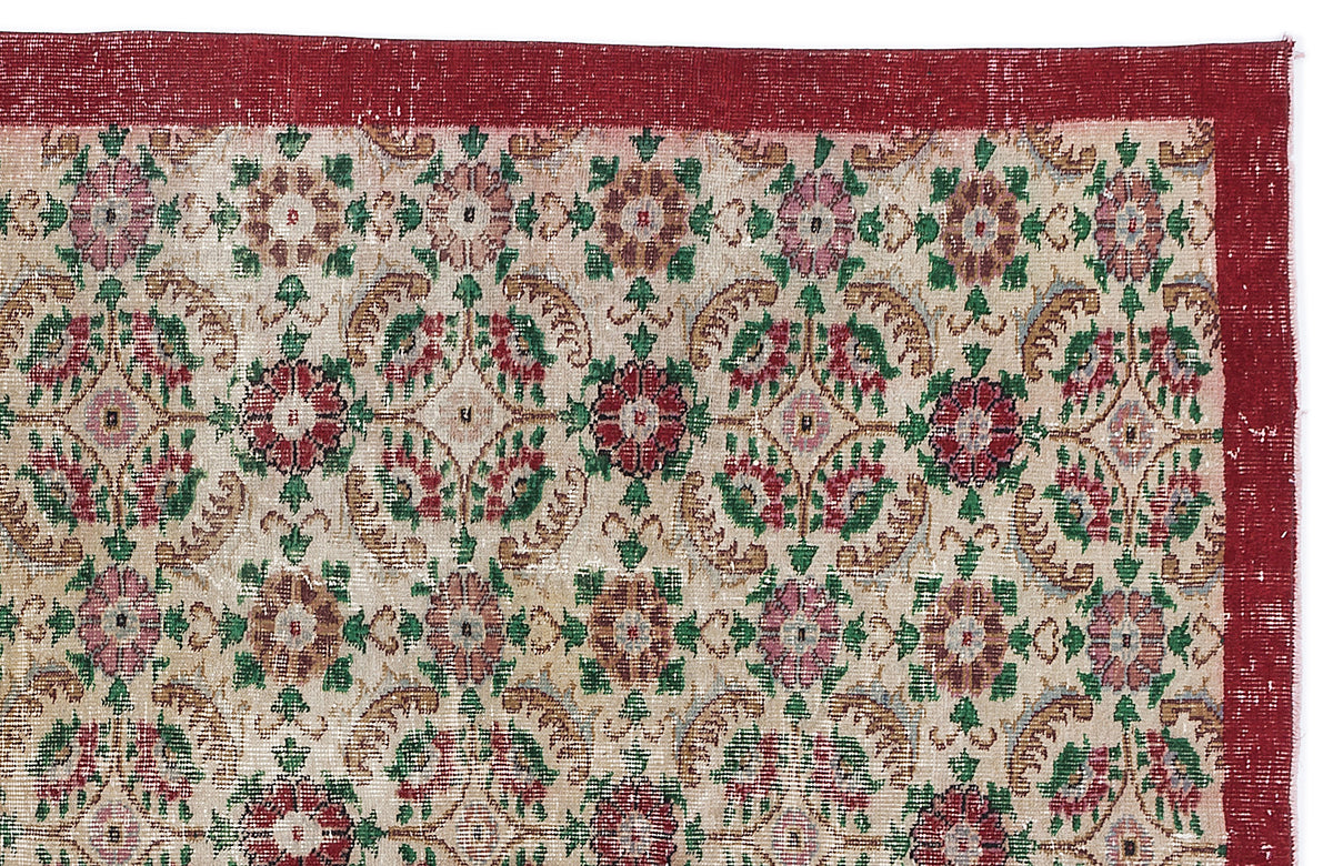 Distressed vintage rug with a red border and a repeating floral medallion pattern in red, green, and beige.