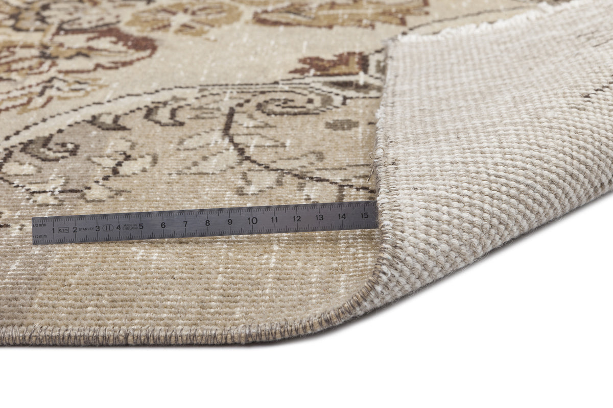 Beige and brown floral patterned rug with a corner folded back to show the woven backing and a metal ruler for scale.