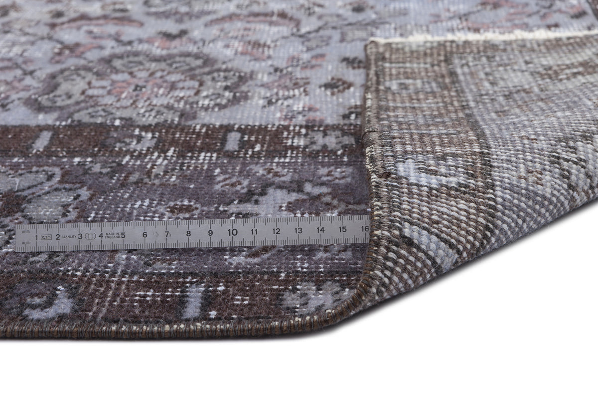 Distressed grey and brown floral medallion rug with a folded corner and a metal ruler for scale.