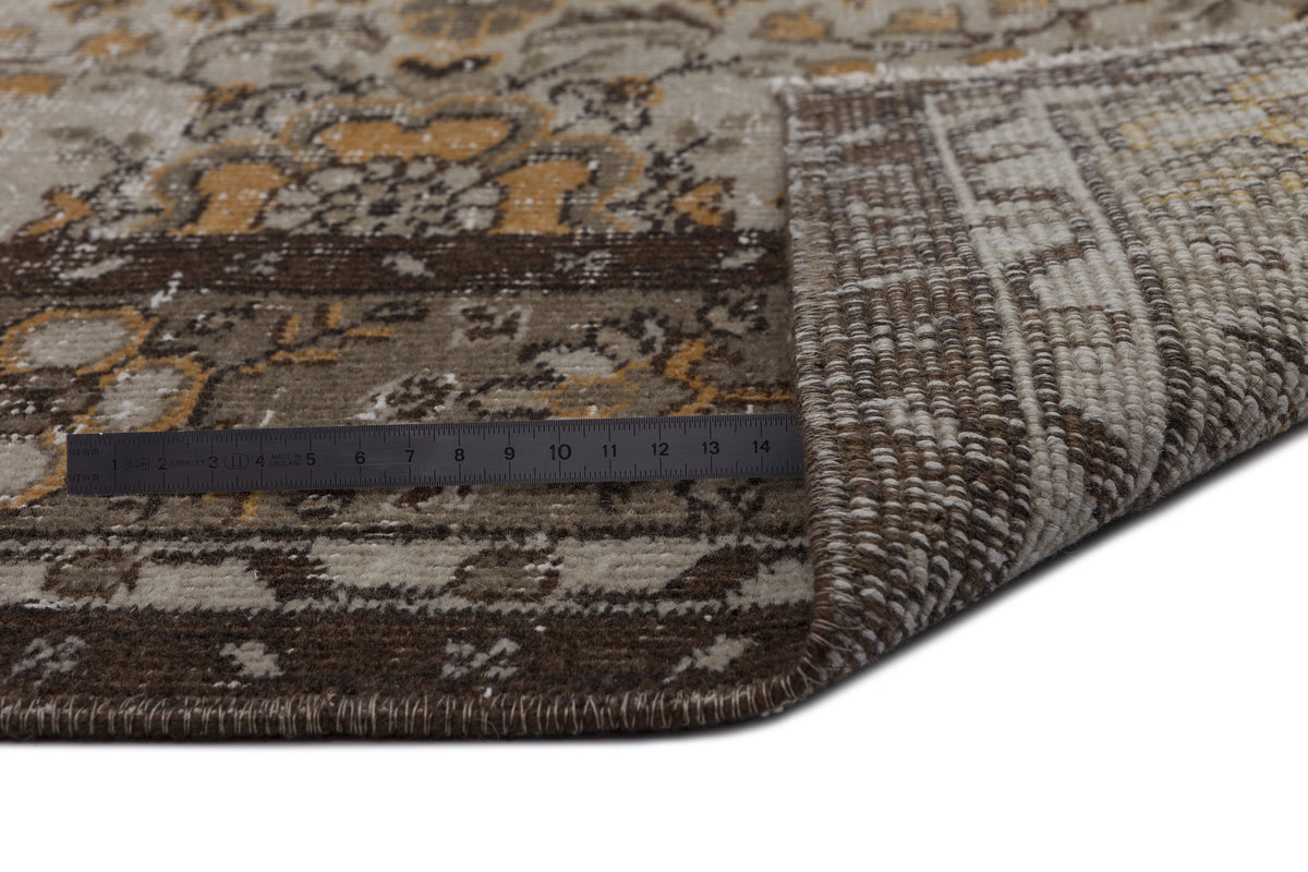 Brown, beige, and ochre traditional medallion rug with a folded corner and a metal ruler for scale.