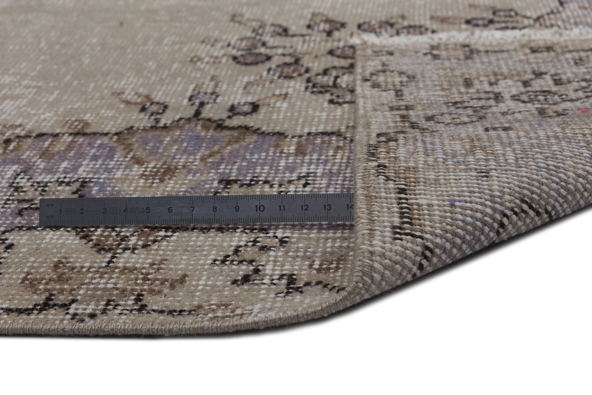 Beige and lavender distressed vintage rug with a floral medallion pattern, shown with a metal ruler for scale.