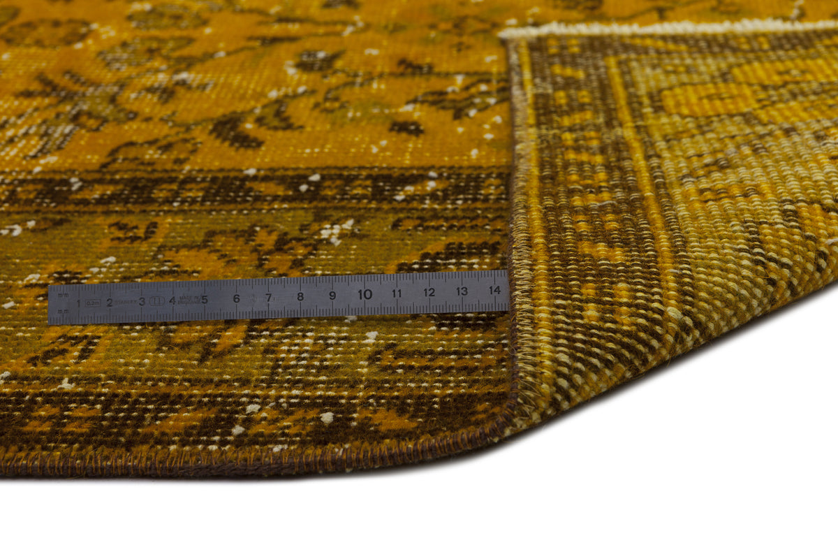 Mustard yellow and brown distressed traditional rug with a floral pattern, shown with a measuring ruler on white.