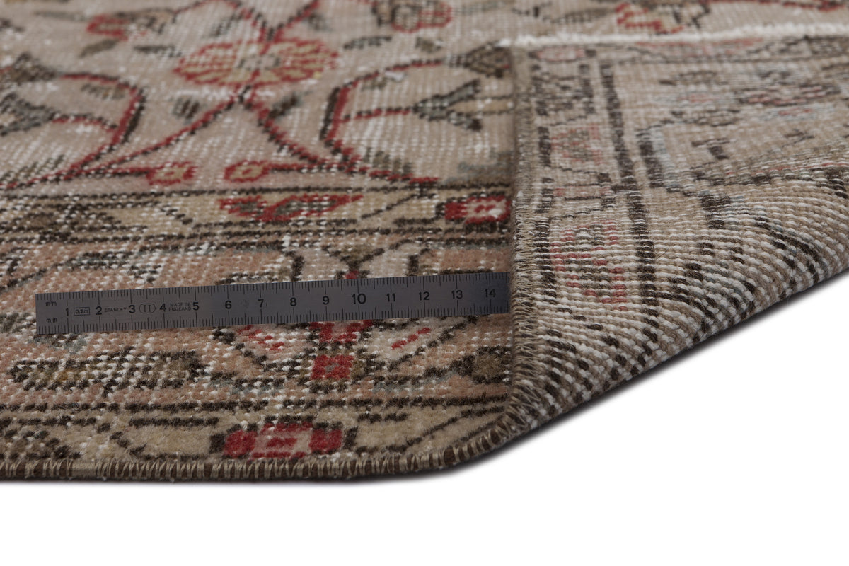 Beige and red traditional floral patterned rug with a folded corner and a metal ruler for scale.