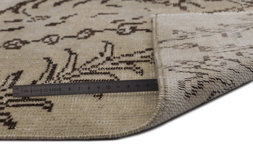 Load image 1 in gallery view. Beige rug with a dark brown abstract pattern, shown folded to reveal the backing with a metal ruler for scale.