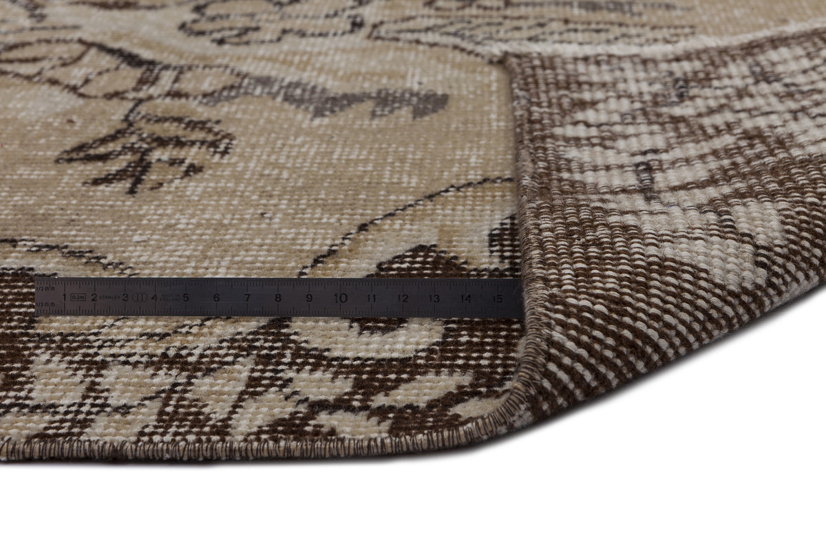 Beige and brown distressed floral rug with a folded corner showing the weave and a metal ruler for scale.