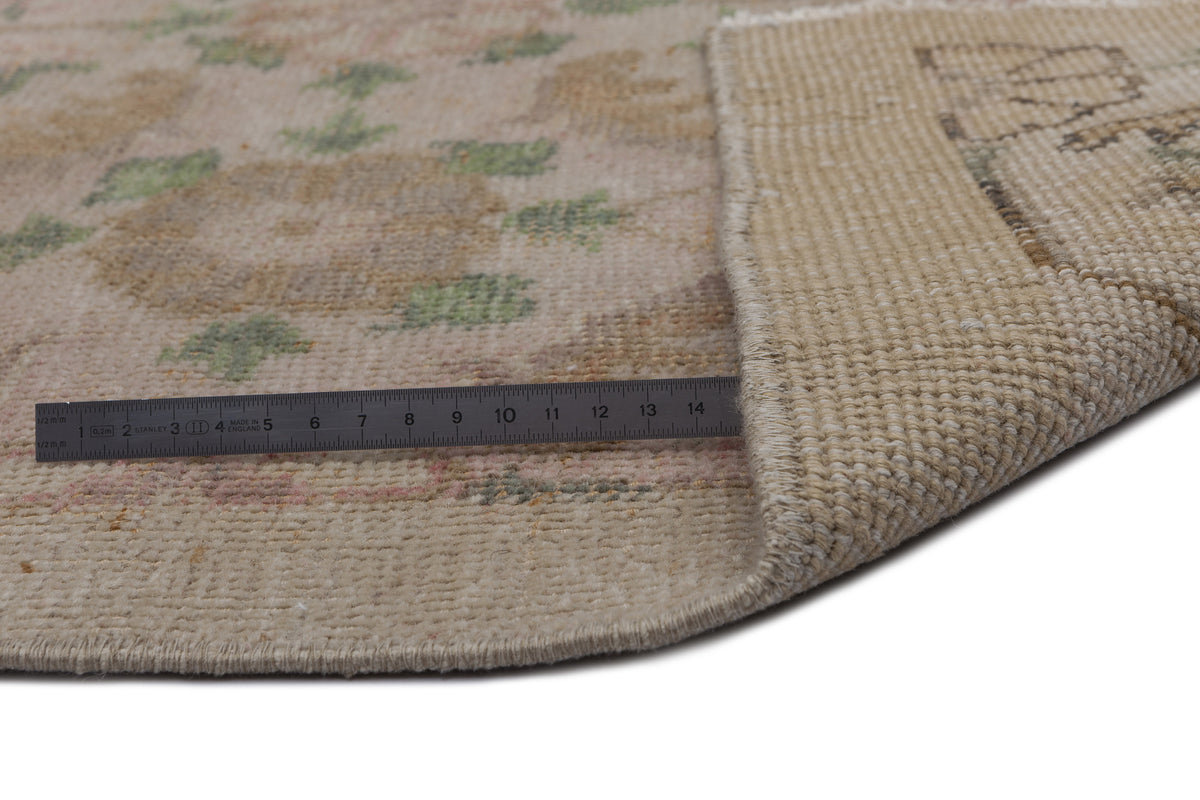 Beige and tan vintage-style rug with a faded floral pattern, shown with a metal ruler measuring the pile and backing.
