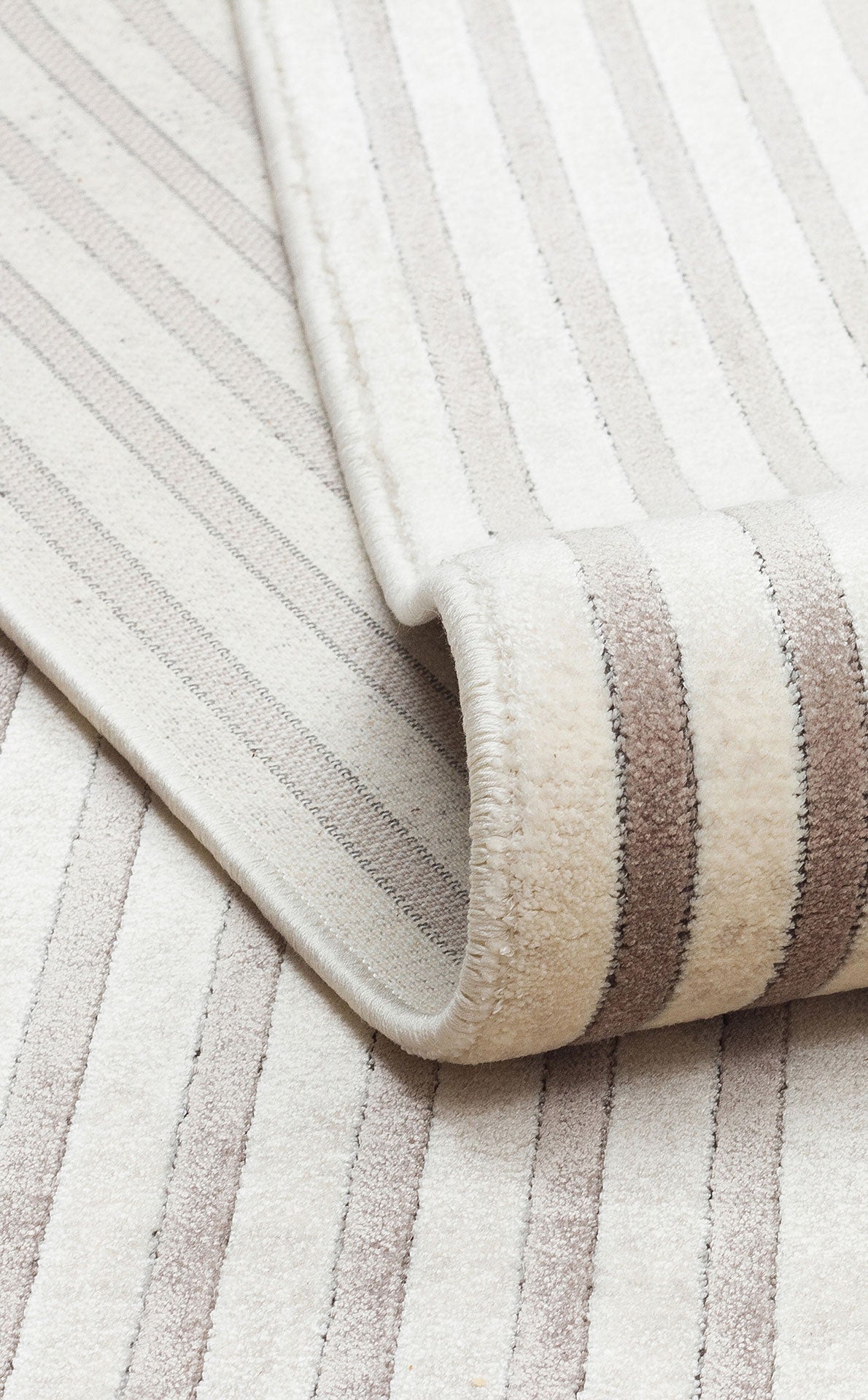 Cream and beige striped rug with a rolled corner showing a thick, textured pile.